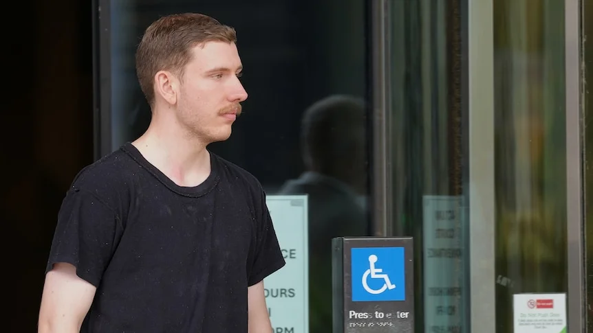 A man with short hair wearing a t-shirt walks out of a court building.
