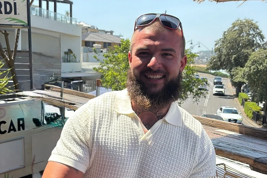 Man with dark facial hair smiling, white shirt, sunglasses on head