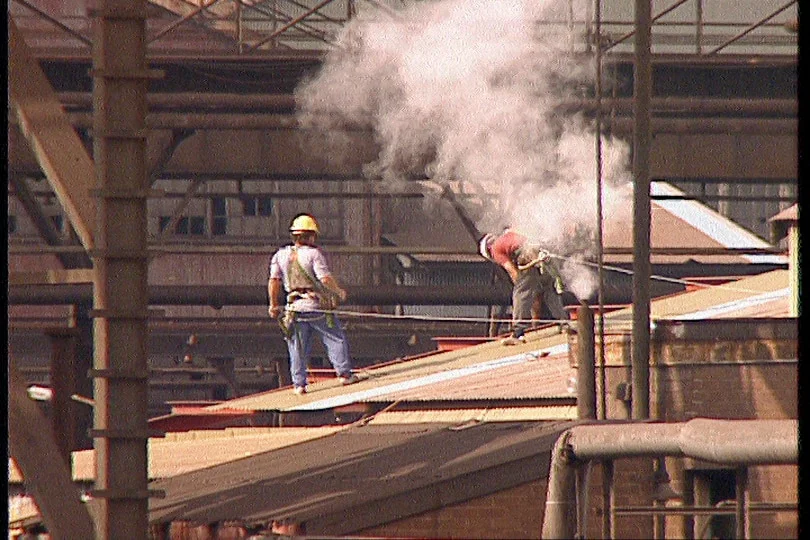 an archival image of two men, dressed in high vis clothes, working at an industrial site