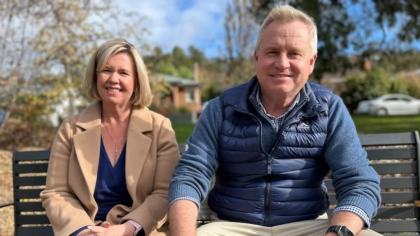 Bridget Archer and Jeremy Rockliff sit next to each other on a park bench.