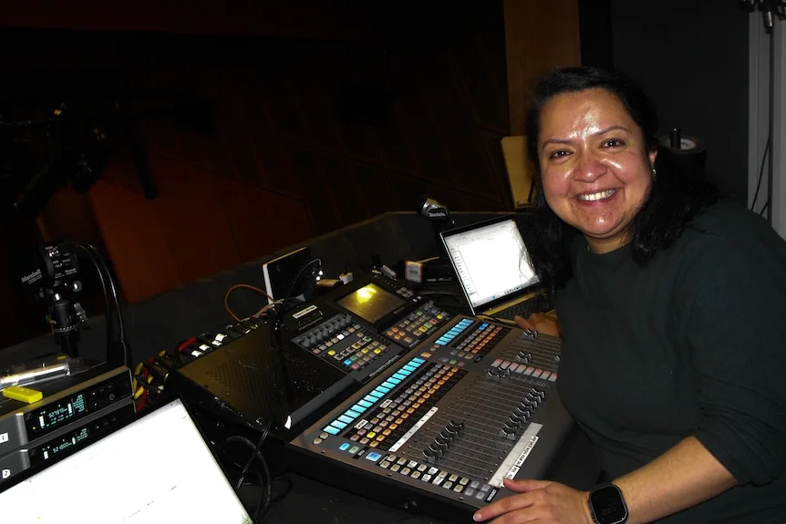 Sunyana sits in front of a console, smiles at the camera.
