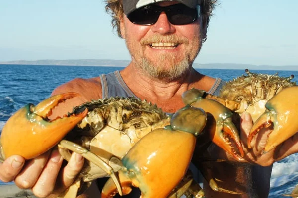 Blonde bearded man holding a mud crab and smiling 