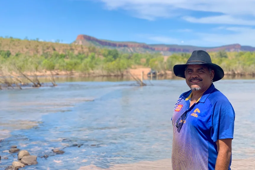 man with black hat in front of river with red mesa cliff formation in background