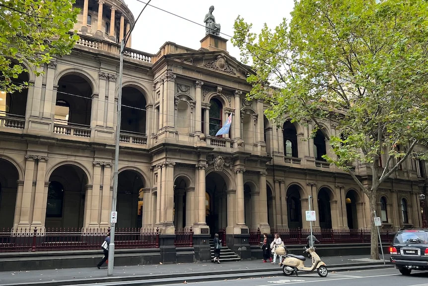 A long distance shot of two people walking past the two-storey Supreme Court building with a statue on the top.