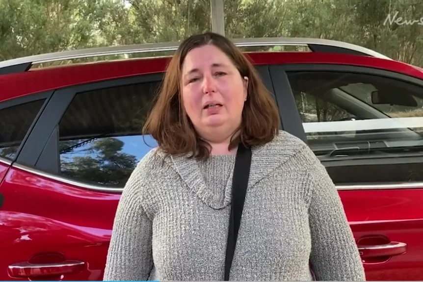 A woman standing in front of her car.