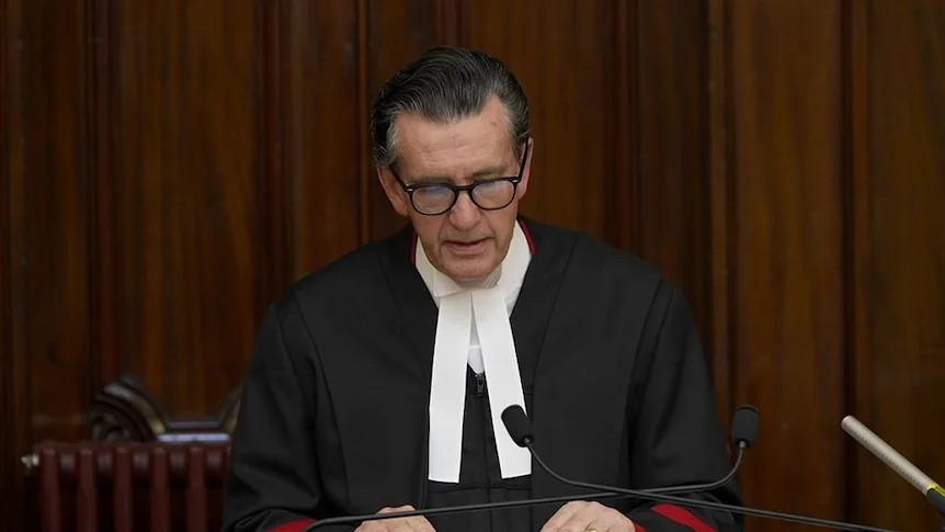 A judge wearing traditional court garb speaks into a microphone.