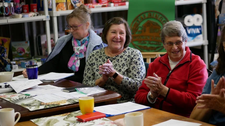 Three ladies at a table, two are clapping and smiling