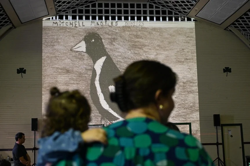Art on a wall with the back of two women's heads.