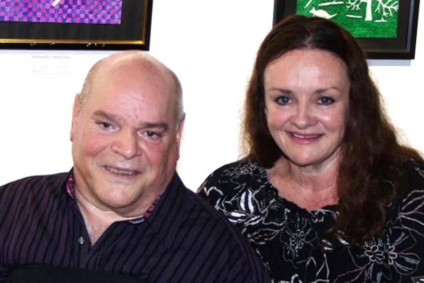 A man and a woman beneath some portrait art.