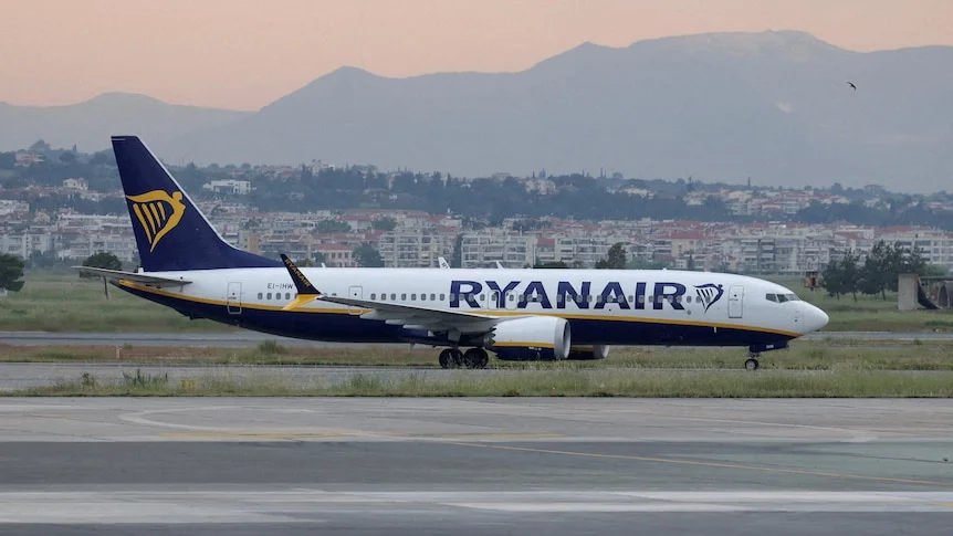 A Ryanair plane sits on the tarmac of an airport with a mountain range in the background.