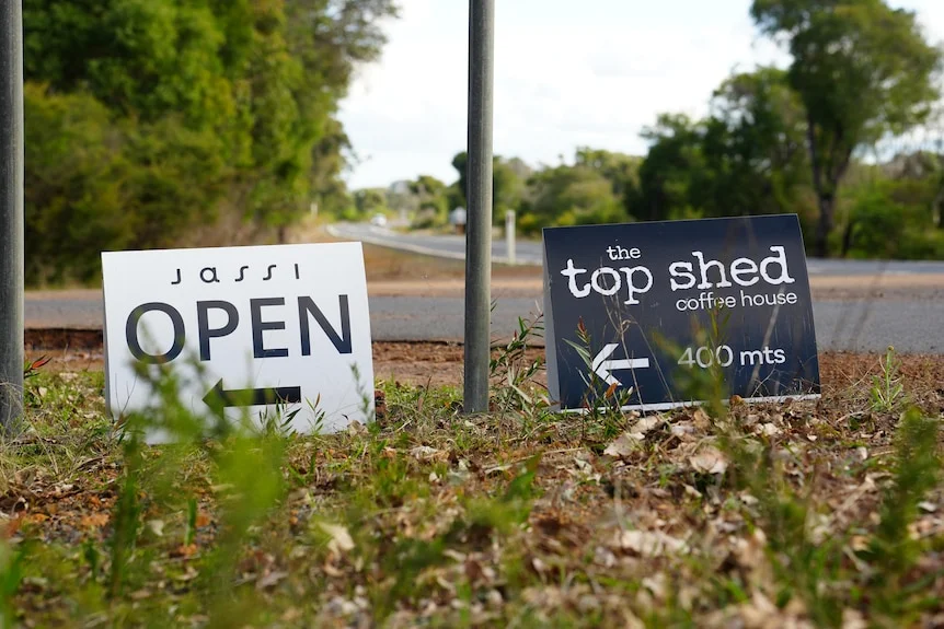 Two small signs on the side of the road with arrows saying open and coffee house.