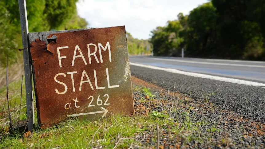 a rusty sign on the side of the road that reads farm stall.
