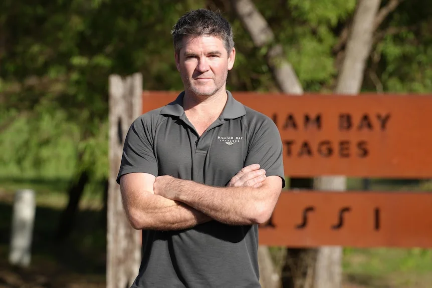 A man in front of a sign with arms crossed.