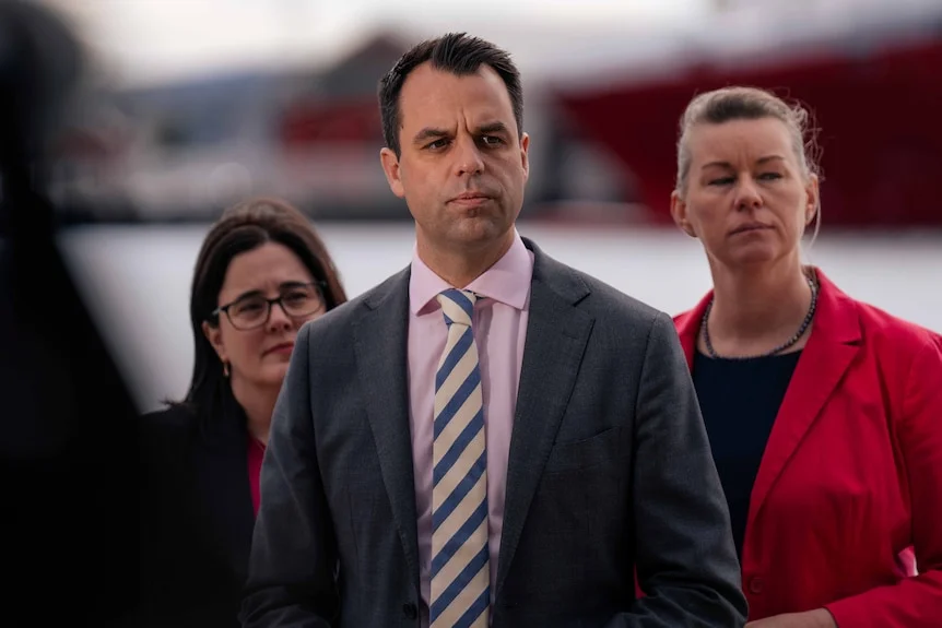 A man speaks at a press conference with two women behind him