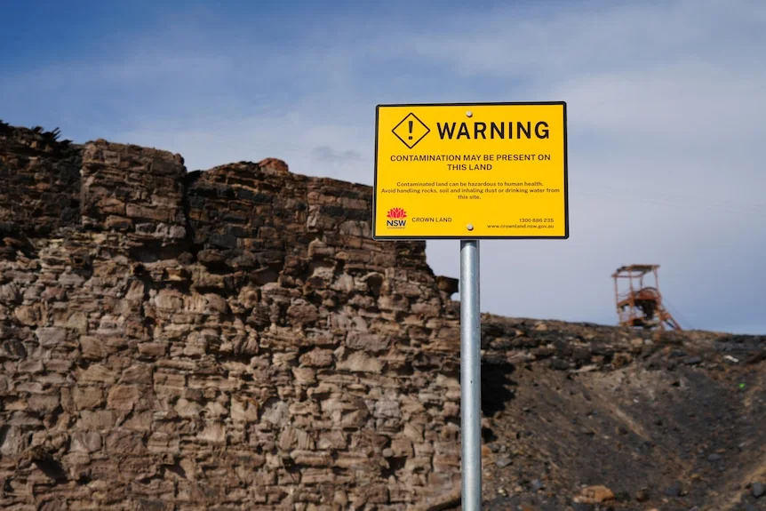 Yellow sign stating "warning contamination may be present on this site" in front of mine wall