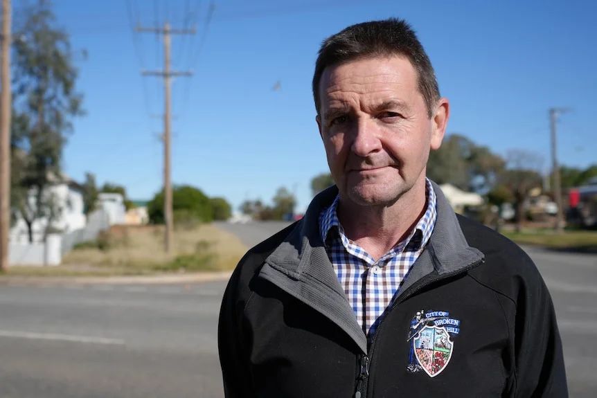 A man standing next to a wide country road, wearing a Broken Hill City Council jacket