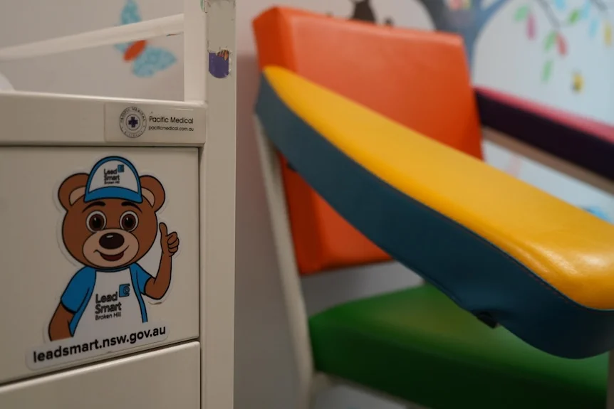 Sticker on drawer of a bear named 'Lead Ted' with a blood testing chair behind it.