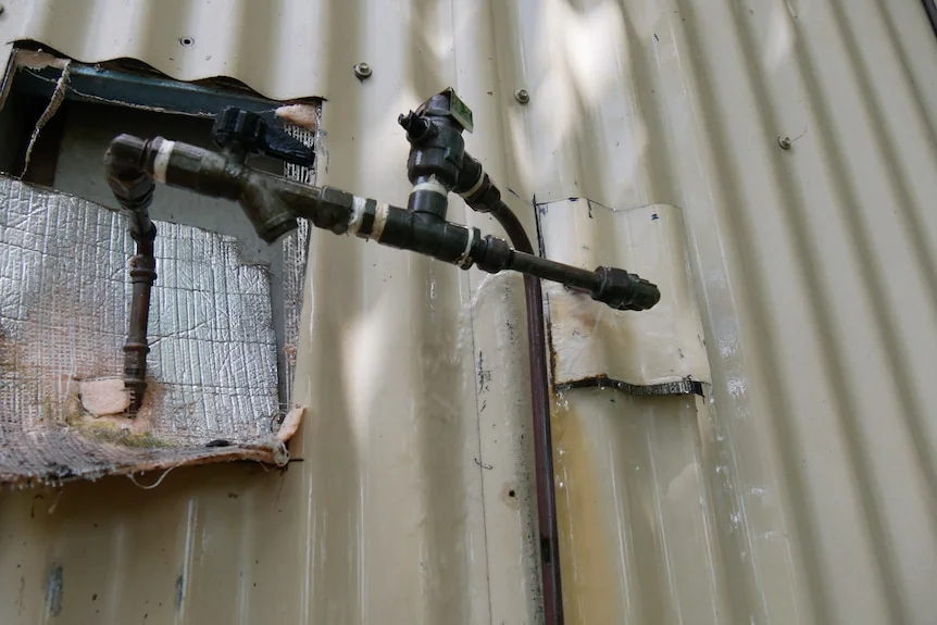 A leaking exterior pipe coming out of a tin wall.