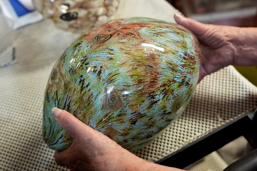 A woman's cups her hands around a predominantly blue and green glass artwork inspired by bush medicine.