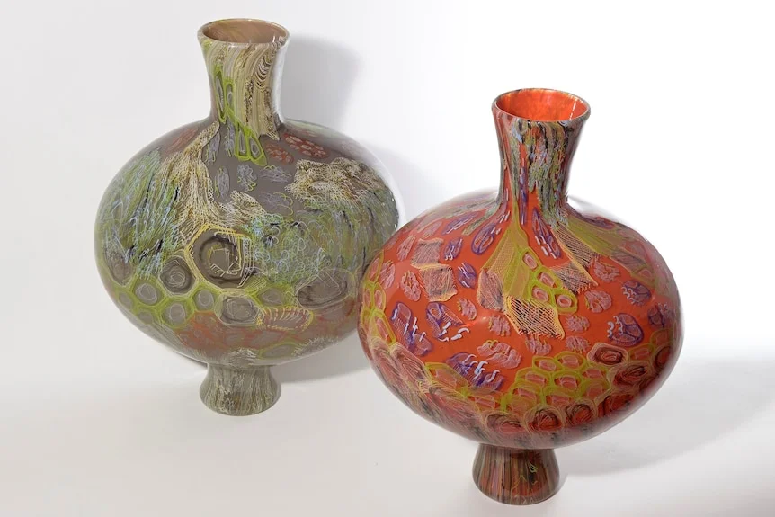 Two bulbous glass vases, one red and one green, both with swirling coloured designs.