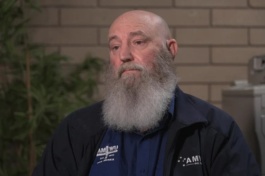 A man with a big grey beard wearing a top and jacket with AMWU emblazoned on it