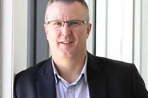 A man with glasses in a blue shirt and jacket. 