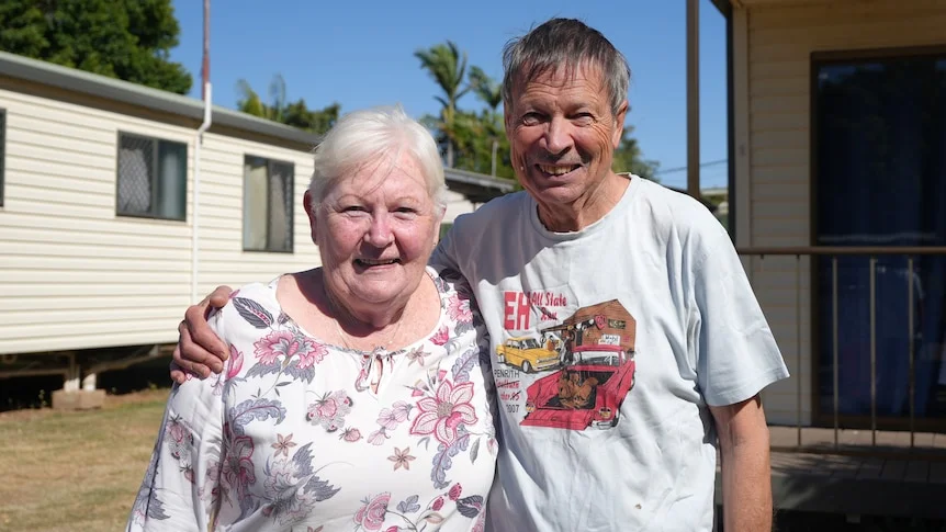 An older couple smile with their arms around each other.