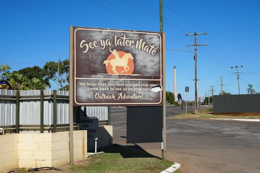 A sign that reads "see ya later mate" at a caravan park, with a blue sky in background.