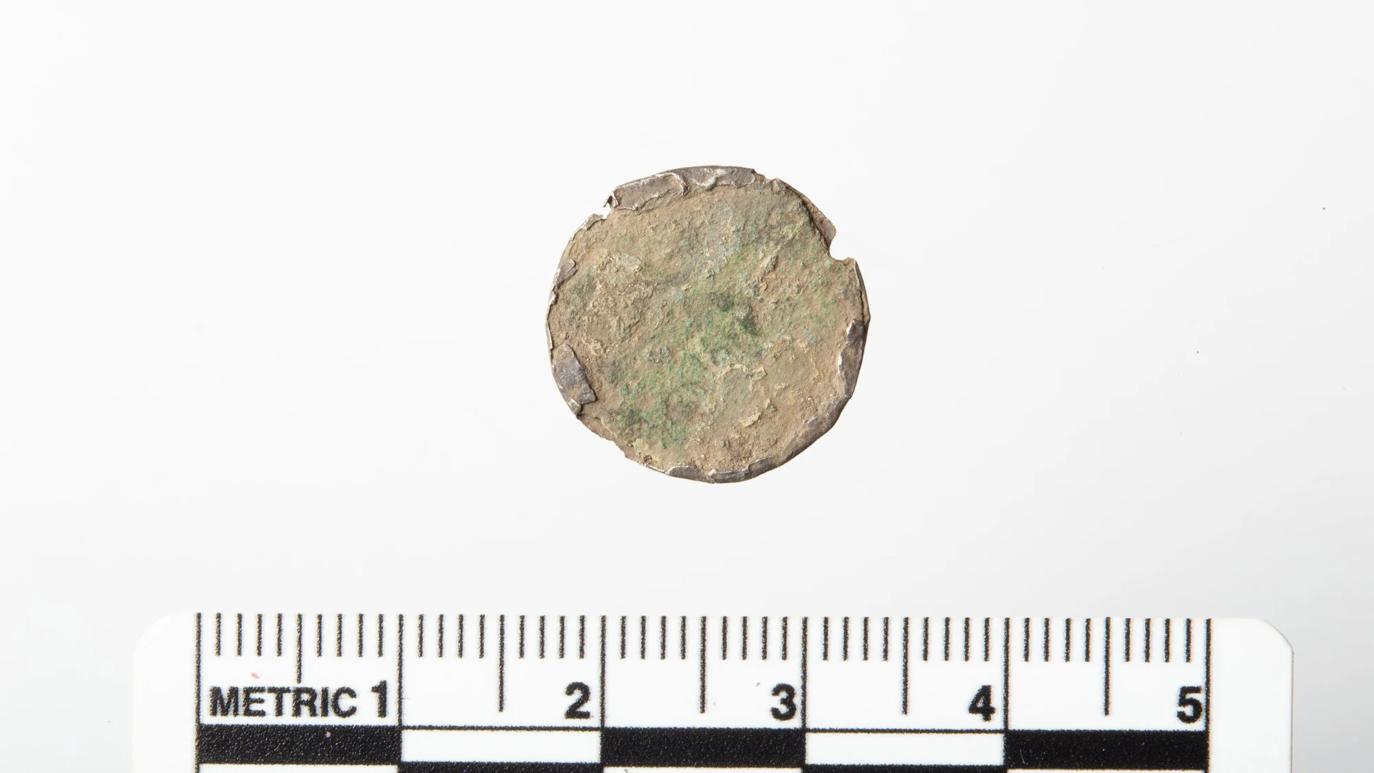 A close up of a copper-colored coin against a white background next to a measuring tape