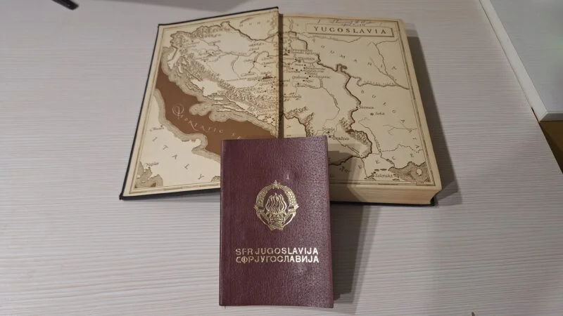 A passport of SFR Yugoslavi and a open book with the map of Yugoslavia. 