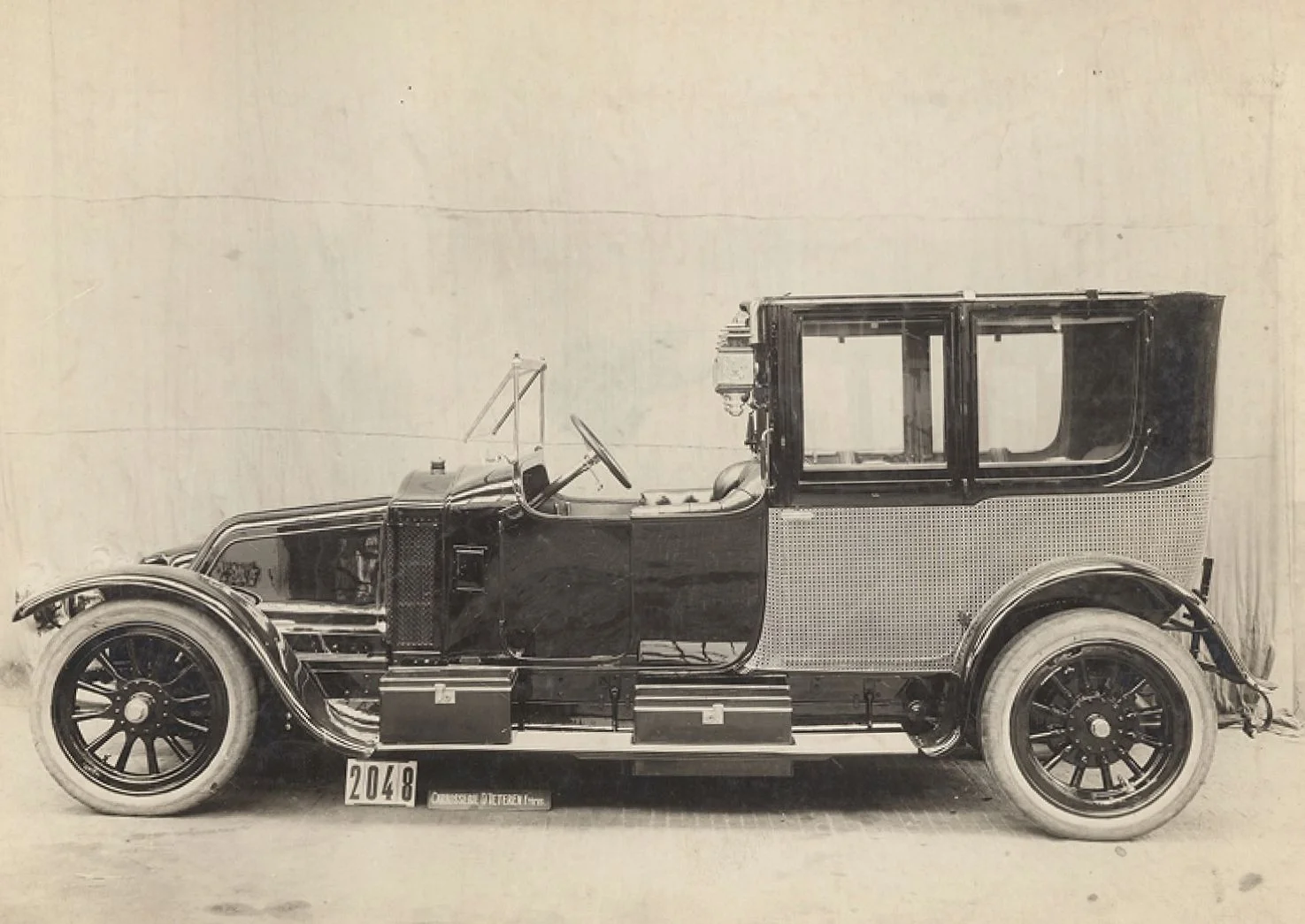 Black and white side view of a vintage D'Ieteren automobile with spoked wheels and a boxy passenger compartment, featuring a 2048 license plate.