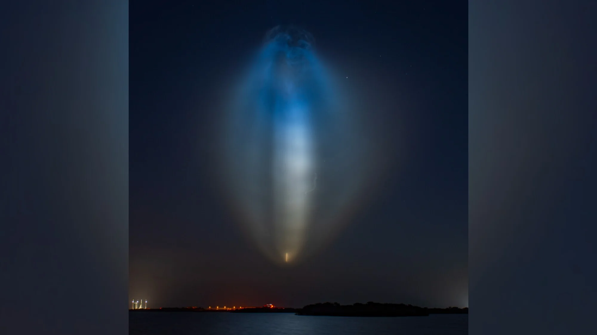 A blue and yellow jellyfish-shaped light shines in the night sky.
