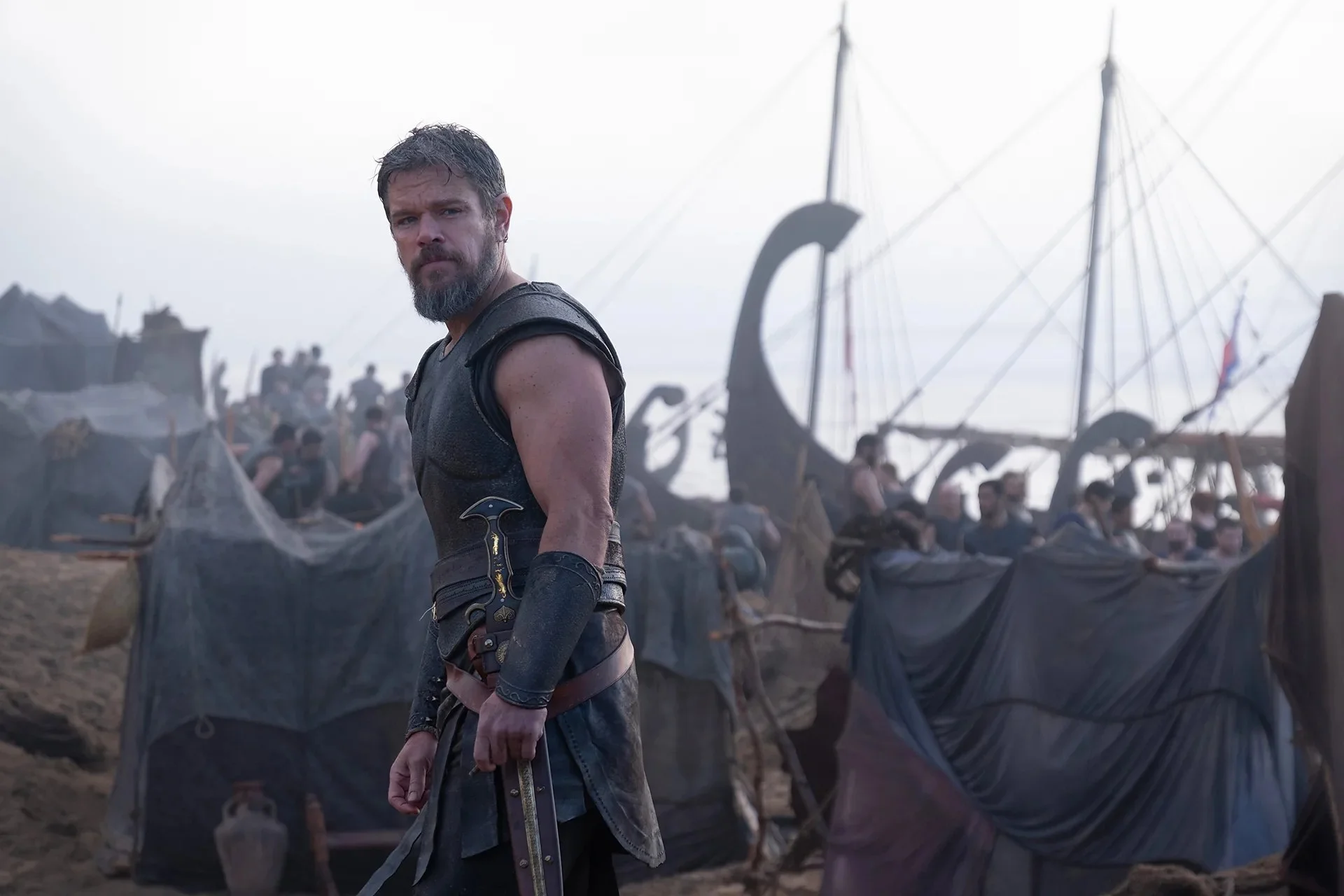 Matt Damon, dressed in Bronze Age armor, stands on a beach in front of a fleet of warships in Christopher Nolan’s The Odyssey.