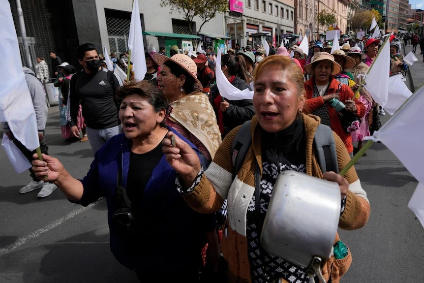 Women hold pots and white flags while walking in a long line.