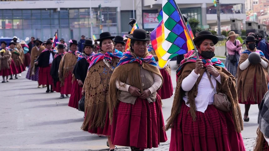 A group of Indigenous women in traditional clothing walking in a line.