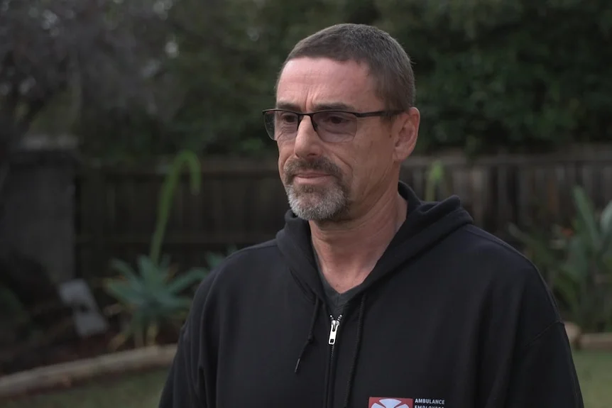 A man in a black jumper speaks in garden to a reporter.