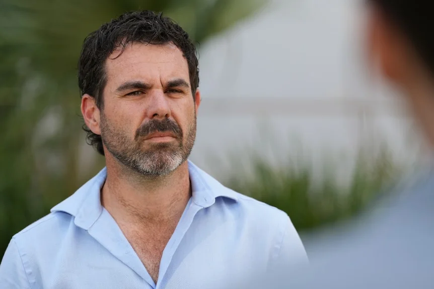 A man with a beard wearing a serious facial expression as he stands outside parliament house.