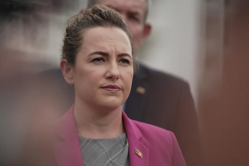 A woman in a pink blazer stares into the middle distance