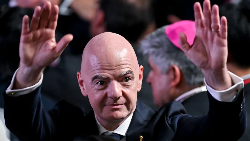 Gianni Infantino stands with both arms raised in the air.