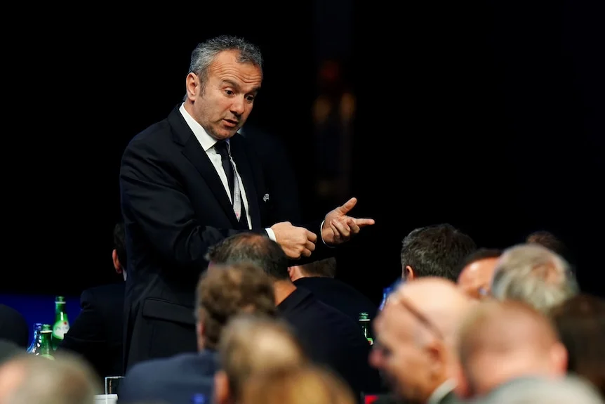 Dejan Savicevic, wearing a suit, stands and motions with his hands while speaking to those seated.