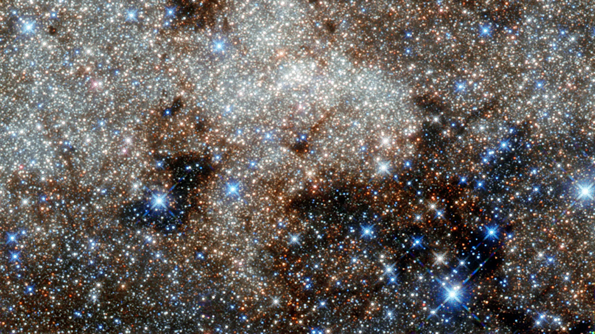 A view of white glowing gas swirling among white and blue stars in deep space.