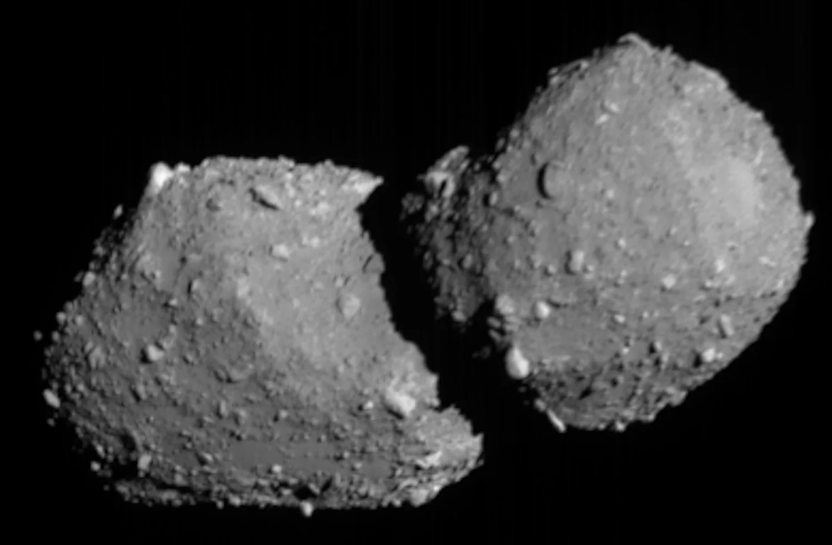 Two rocky asteroid segments with rough, cratered surfaces appear to be touching or fused together against a black background, resembling an early stage in dirty snowball planet form.