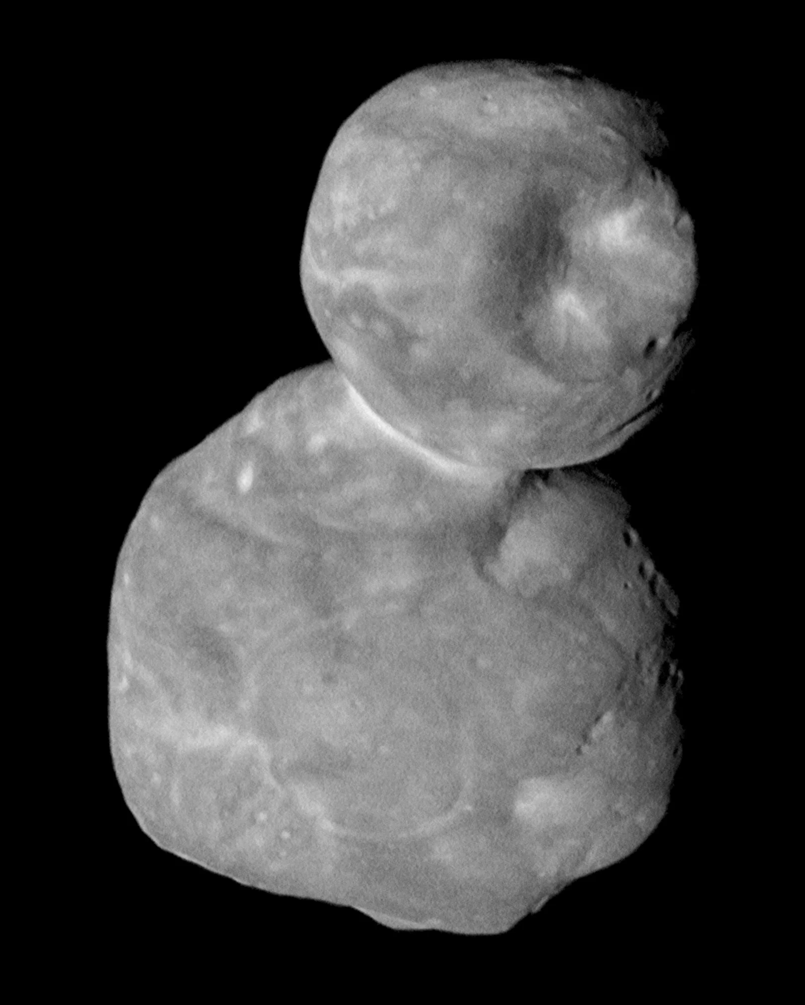 A grayscale image shows a two-lobed object in space, resembling a classic “dirty snowball planet form,” with a smaller, rounded lobe on top of a larger, irregular lobe, set against a black background.