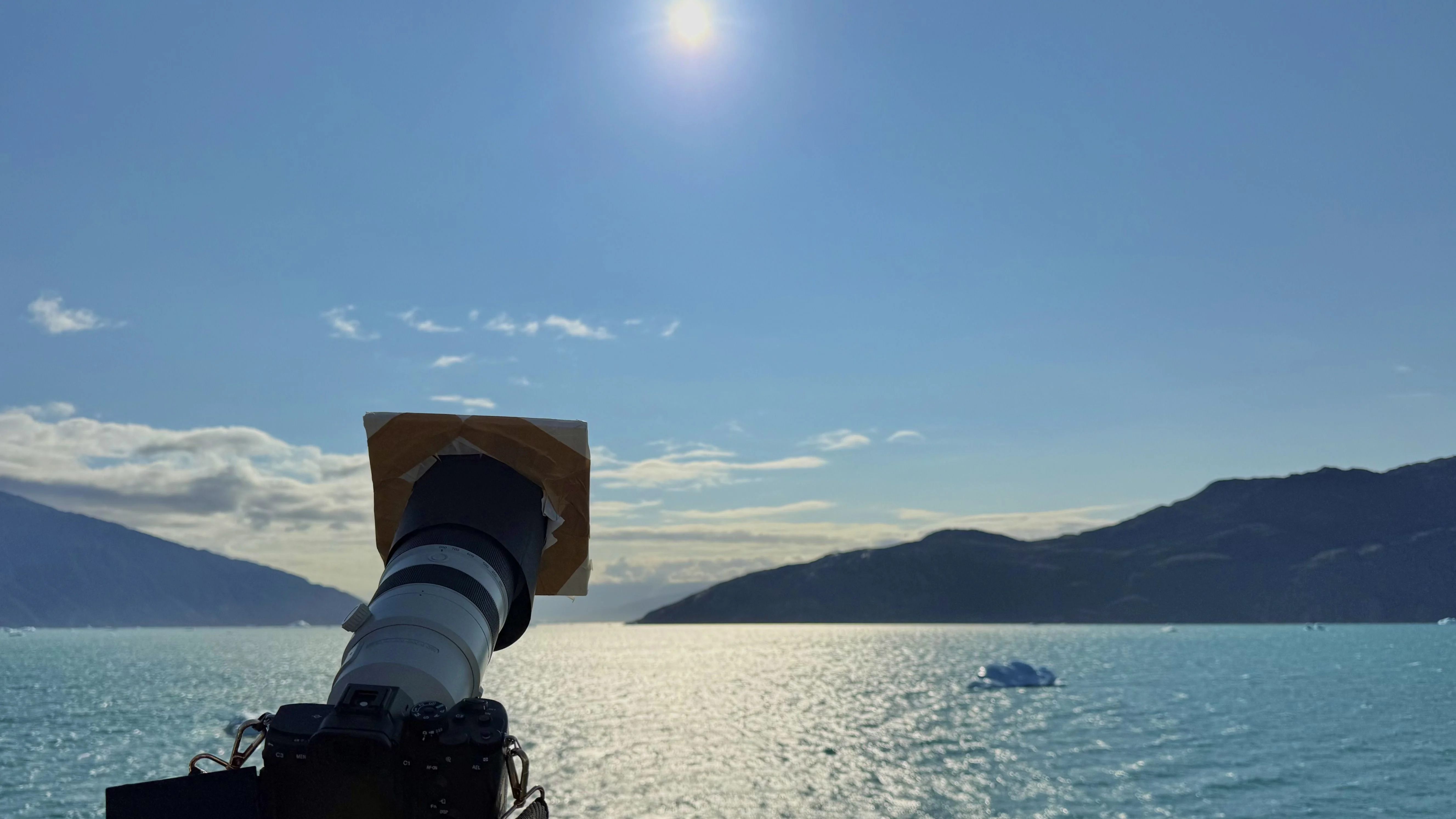 a camera on a tripod and a solar filter point at the sun from the deck of a ship