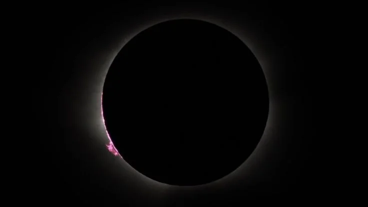 close up view of the suns chromosphere appearing as a thin pink disk and a large prominence at the lower left corner
