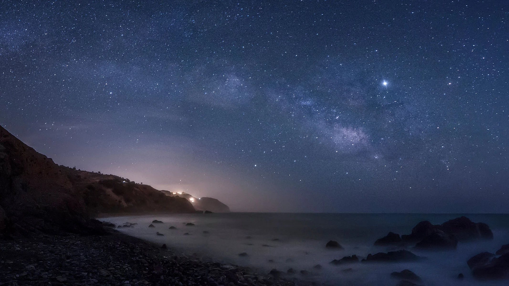 Milky Way stretching over a coast line with many stars and planets visible