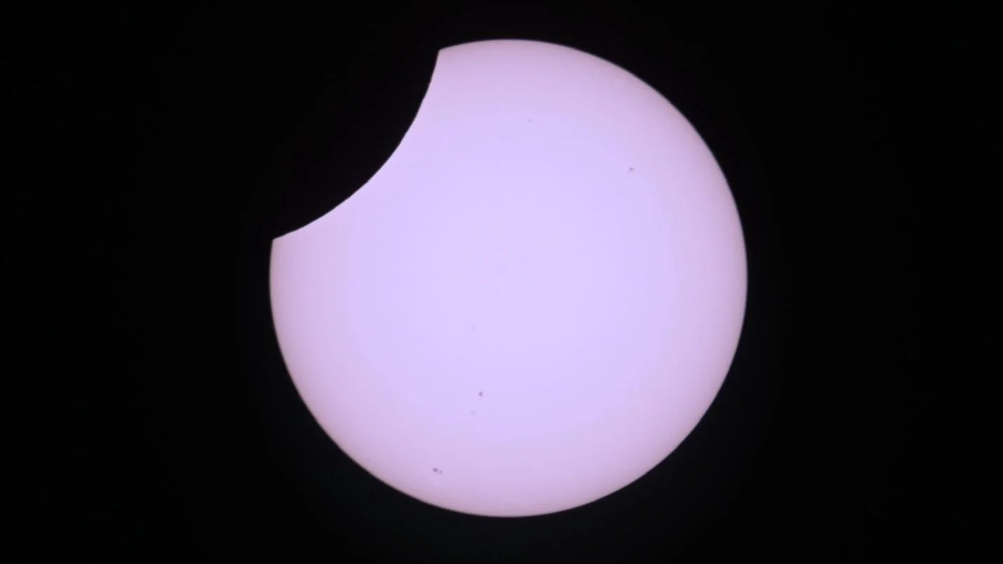 The sun's partially eclipsed disk is pictured in a black sky as the moon's curved silhouette hides a portion of its upper left segment.