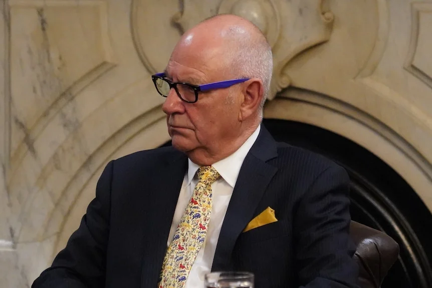 A bald man wearing a suit and tie with a pocket square