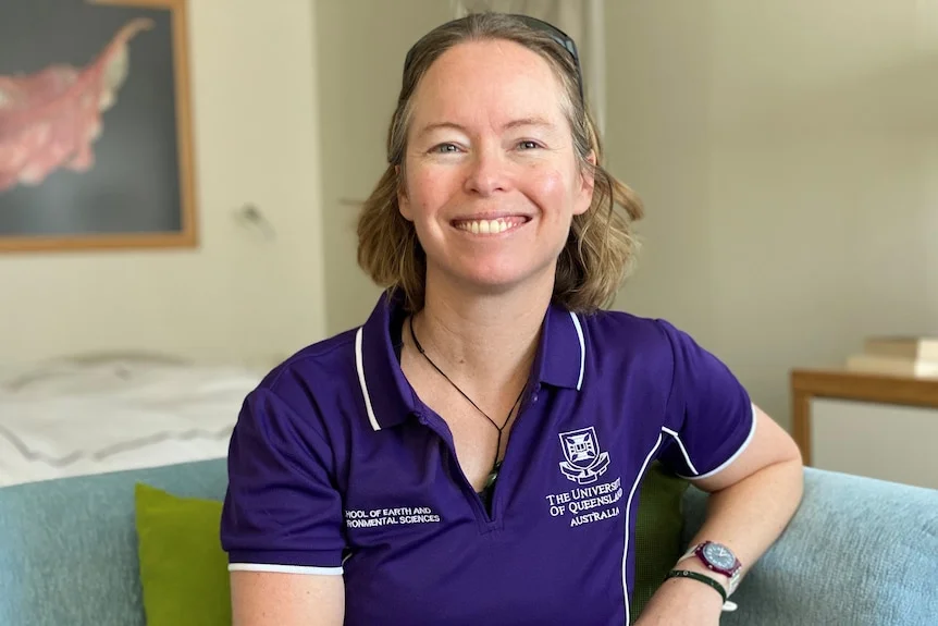 A woman sitting in a purple polo shirt smiling