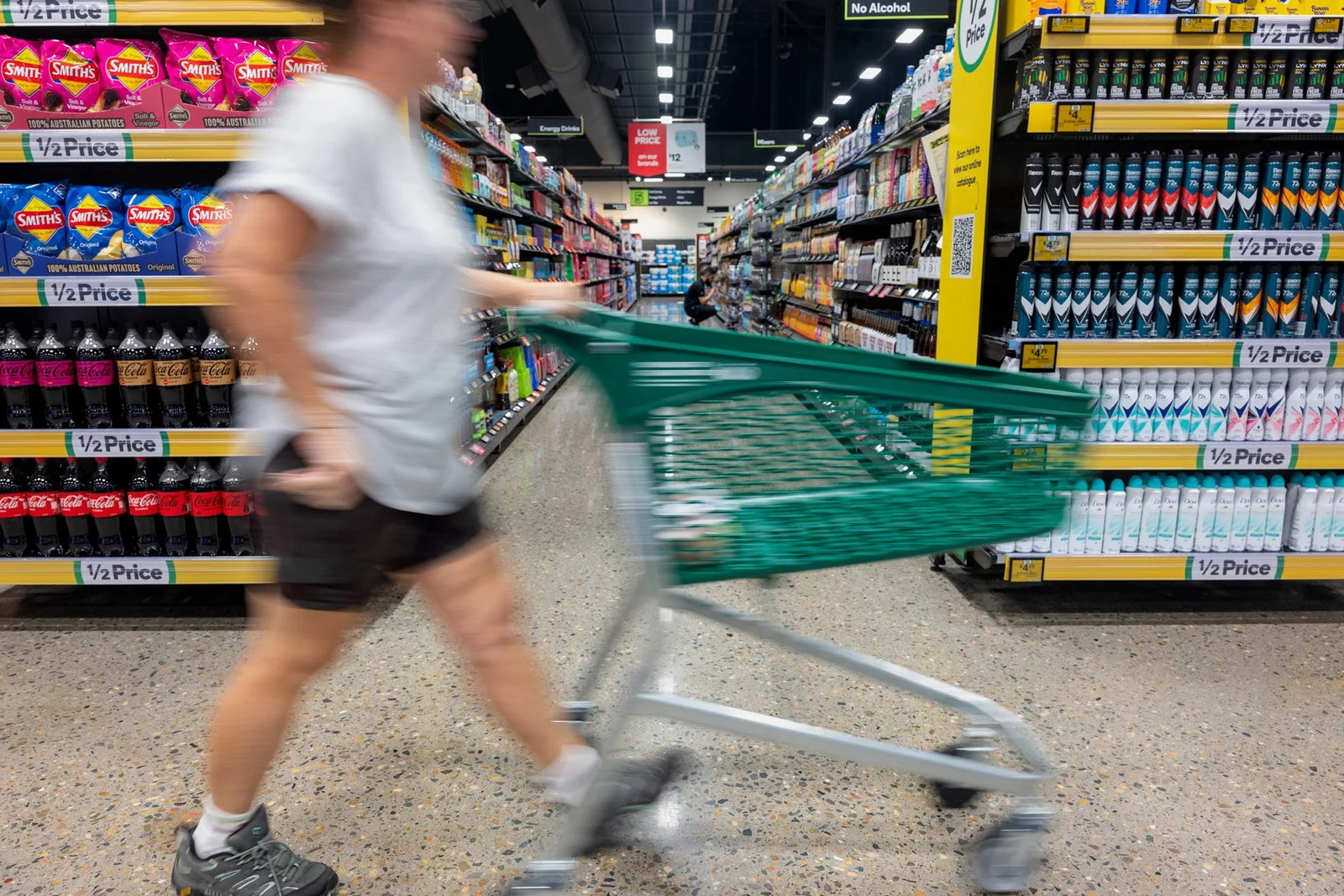 A person walking through a supermarket with a green trolley. 